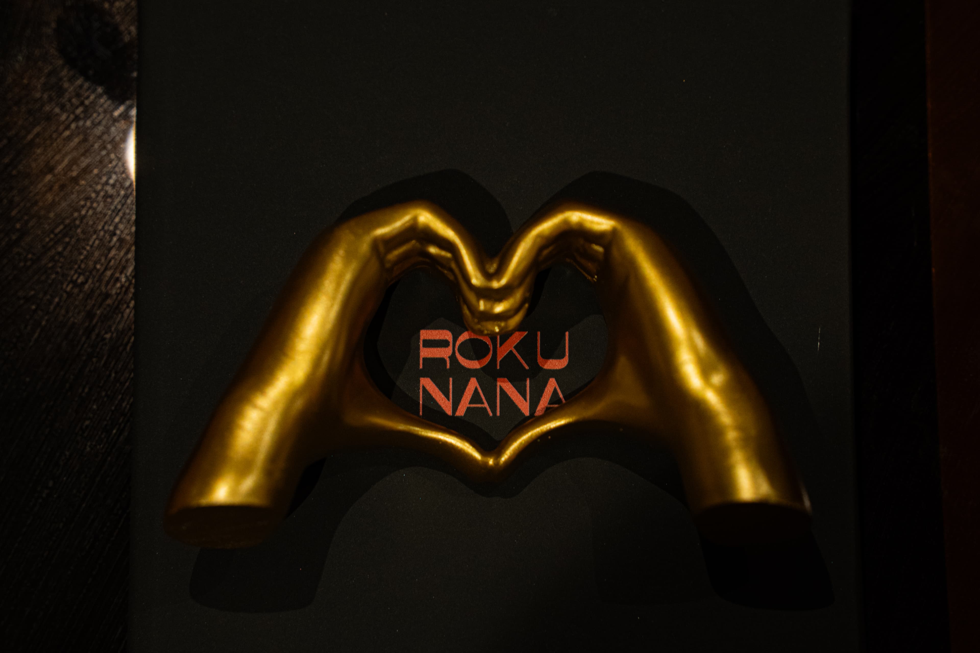 Gold heart hands sculpture framing ROKU NANA logo at 67 Clinton St, NYC